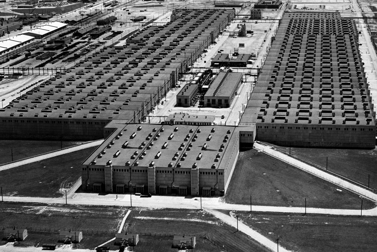 An aerial view of 3 large buildings surrounded by protective fencing.