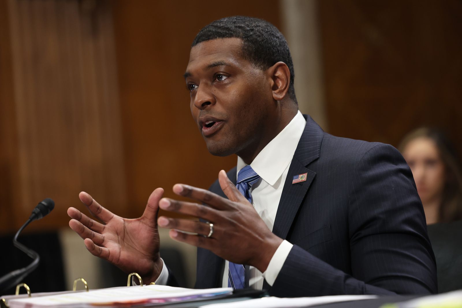 Man wearing a suit speaking into a microphone while seated