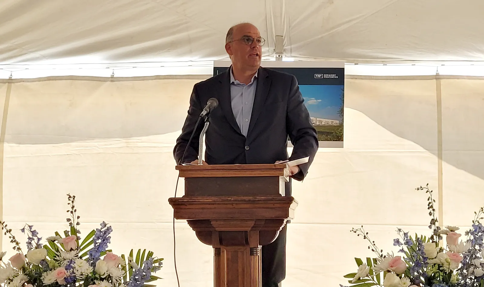 A person speaks from behind a podium while in a white tent.