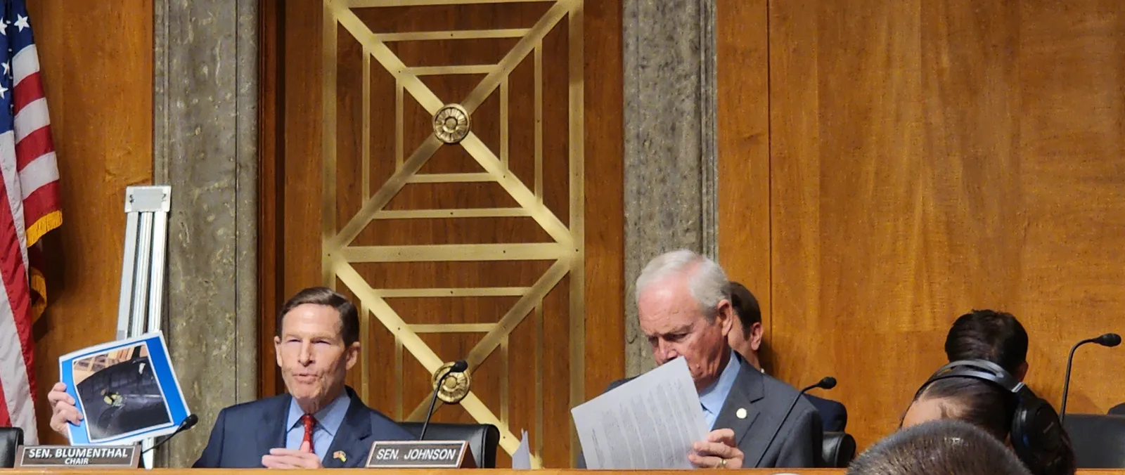 Two people in suits, one of whom is holding up an image.