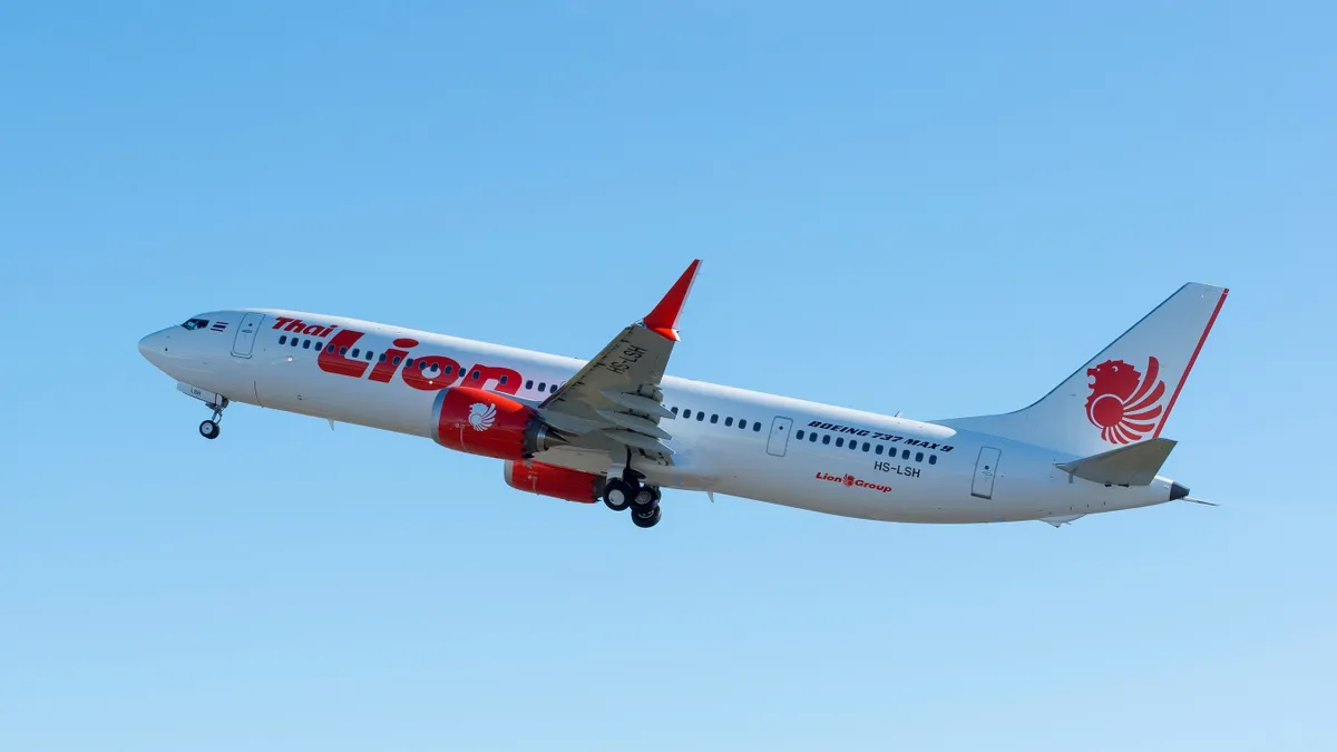 An aircraft flying in the sky with the red Thai Lion Air logo.