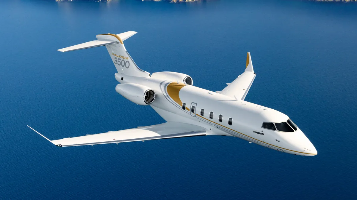 A Bombardier passenger aircraft flies over the ocean with a strip of land visible.