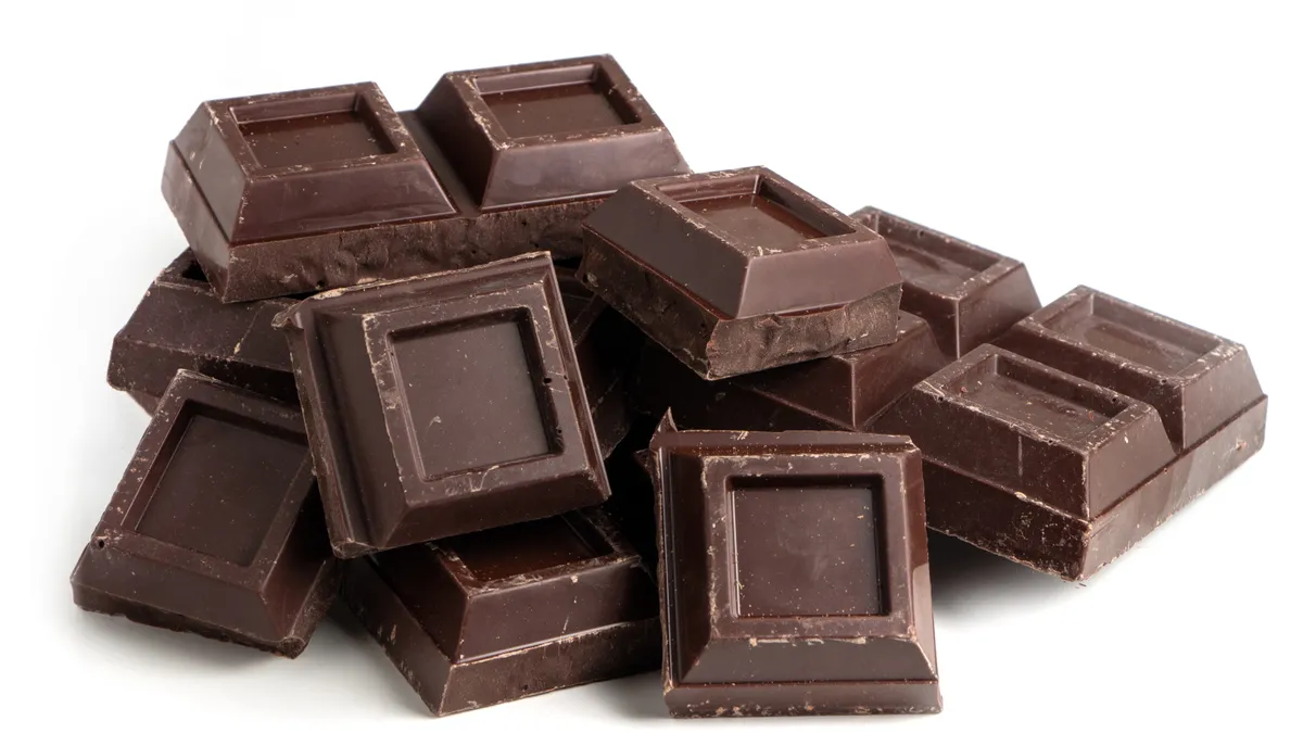 Broken squares of dark chocolate in a pile on a white background.