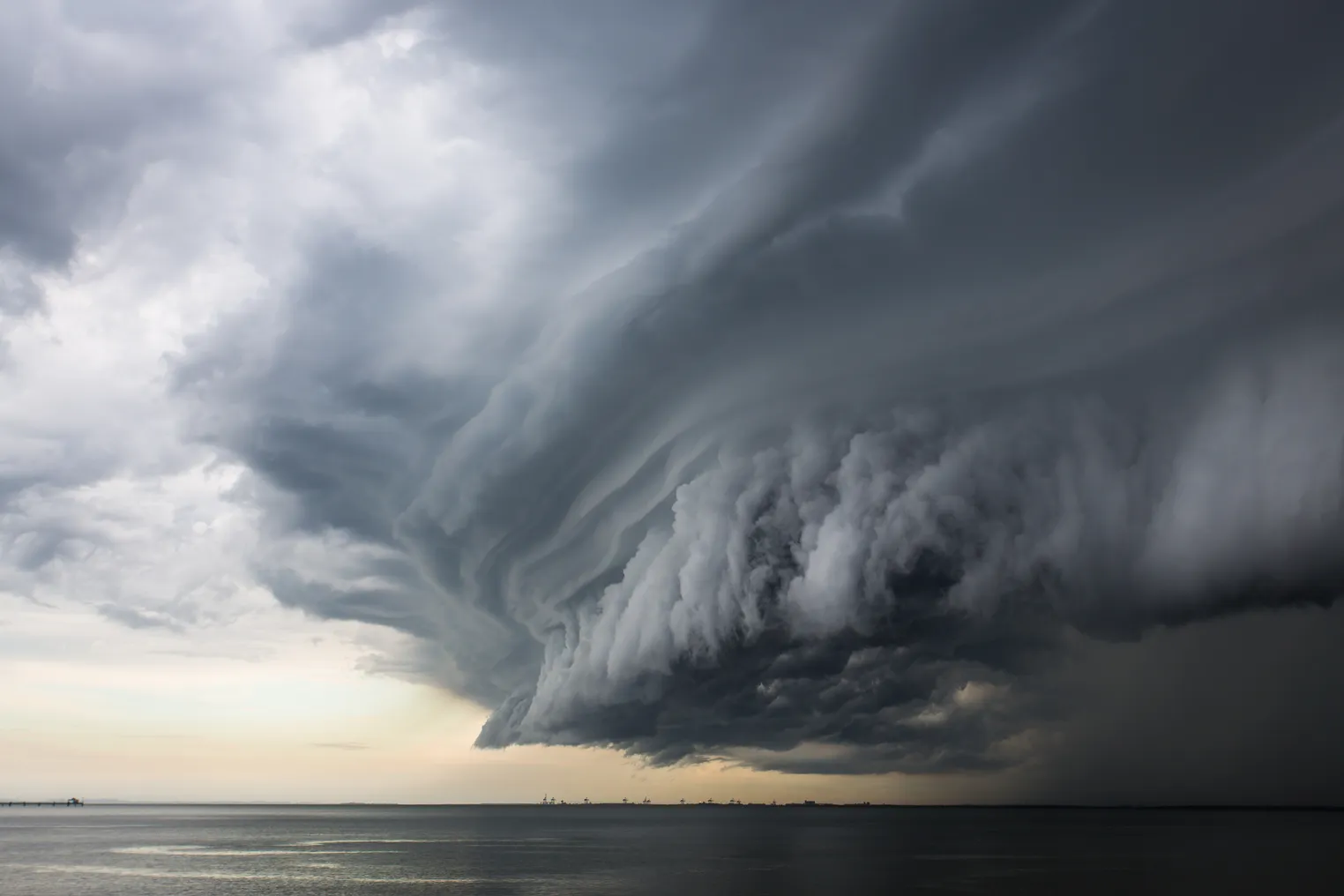 A massive gray storm cloud gathers on the horizon over a placid body of water.