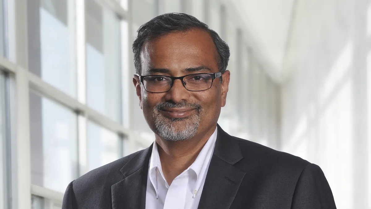 A headshot of a person wearing glasses and a gray business suit.