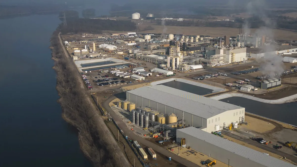 An aerial view of a industrial plant that sits along a river with a smoky horizon.