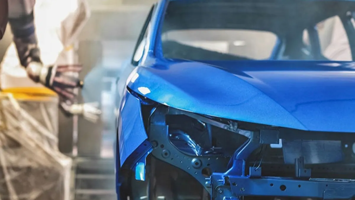 The exterior of a car being painted blue by a robot in a factory.