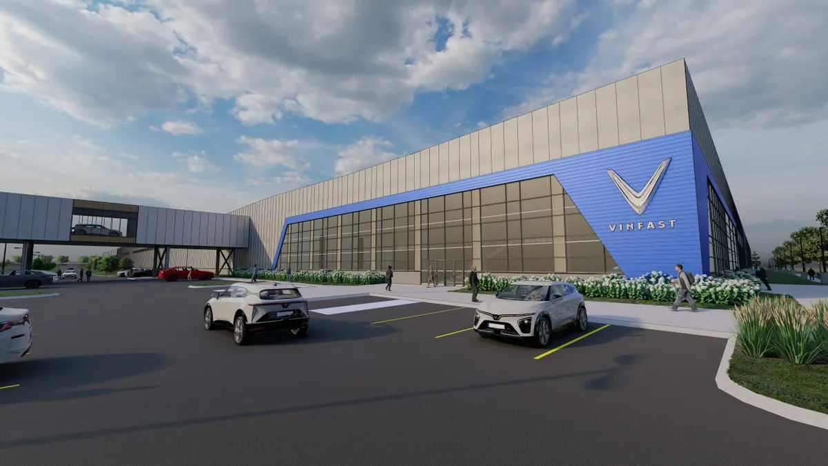 A rendering of a silver building with the Vinfast logo on a baby blue background, with a parking lot in front of it.